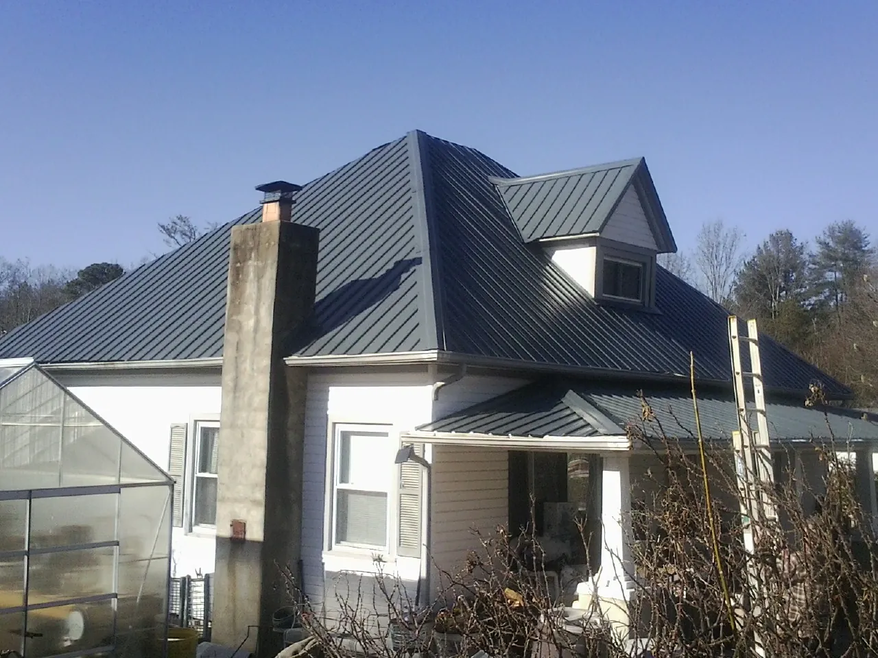 Dark blue standing seam metal roof on a white farmhouse with dormer — Slate & Tile Roof Repair by Roofing Brothers in De Borgia