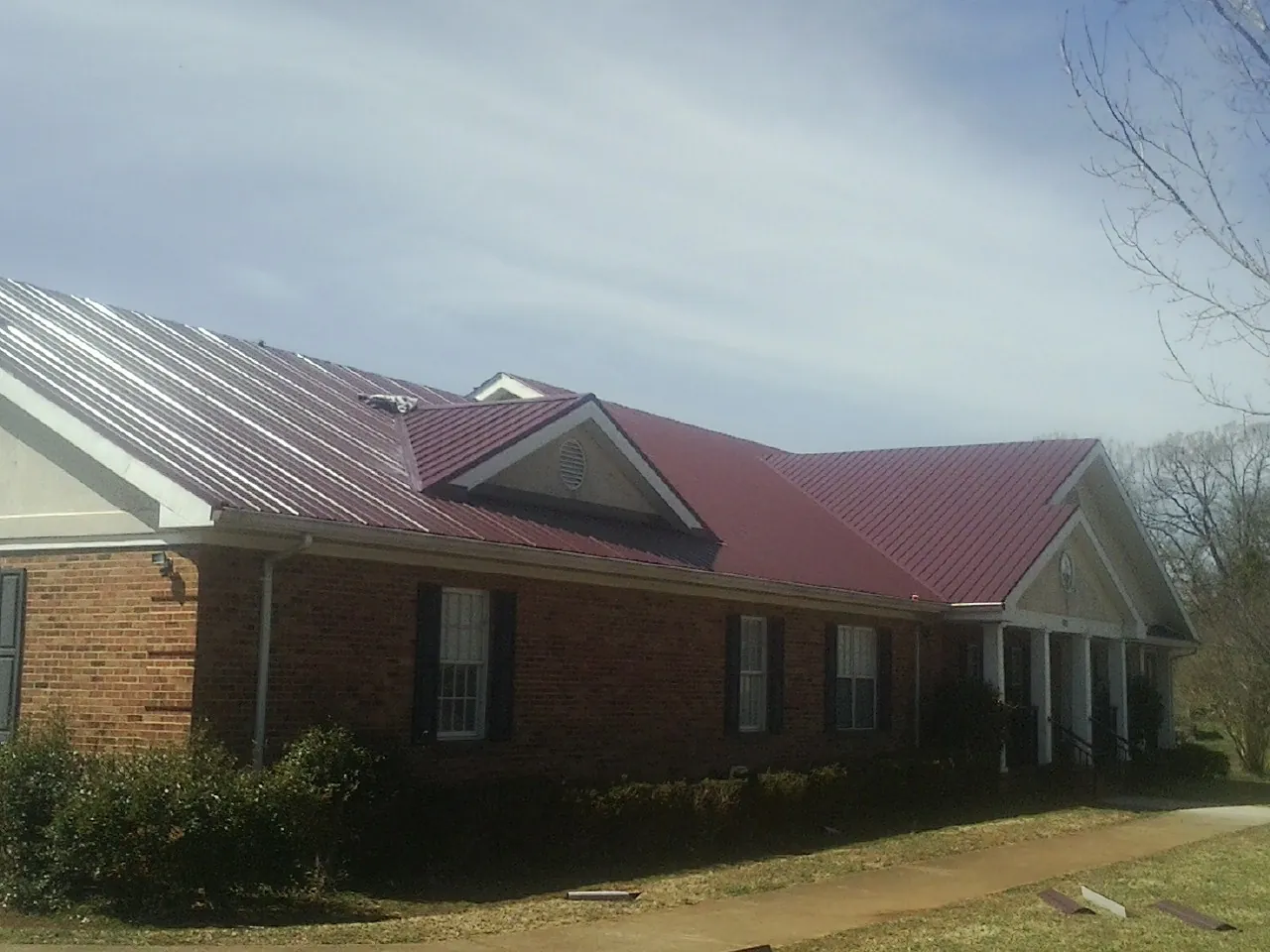 Red metal roof with gabled entries on a long brick building, from a Hail Damage Roof Repair job in De Borgia