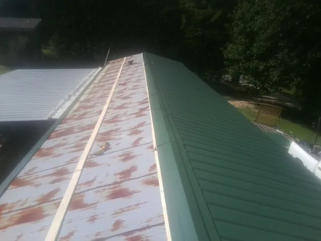 Old rusted panels beside newly installed green metal roofing in De Borgia