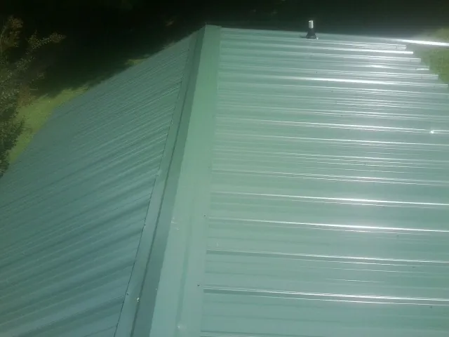 New green metal panels meeting at the ridge of a roof — Flat Roof Repair work by our crew in De Borgia
