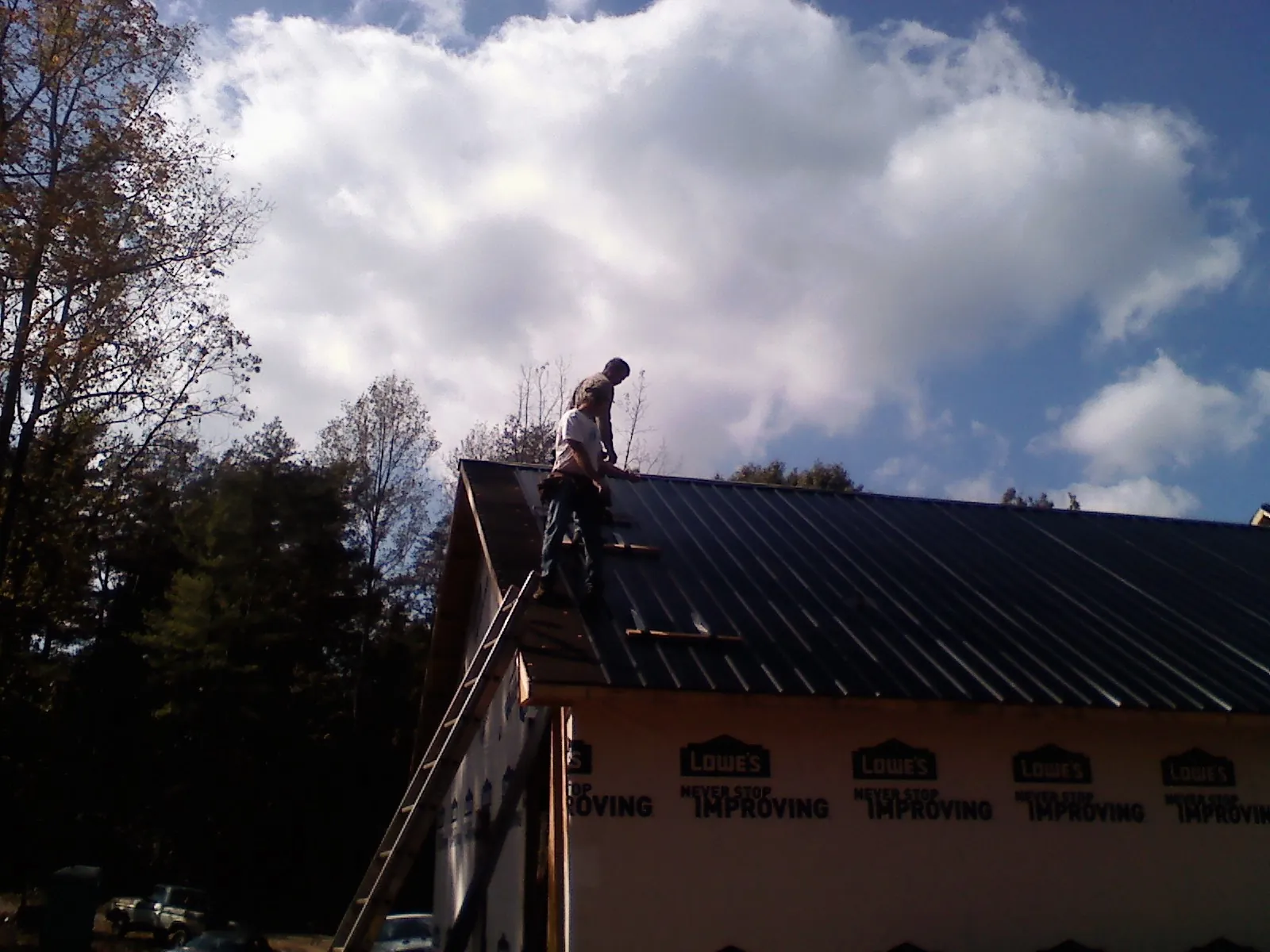 Roofer fastening dark metal panels high against a cloudy sky, from a Roof Inspection job in De Borgia