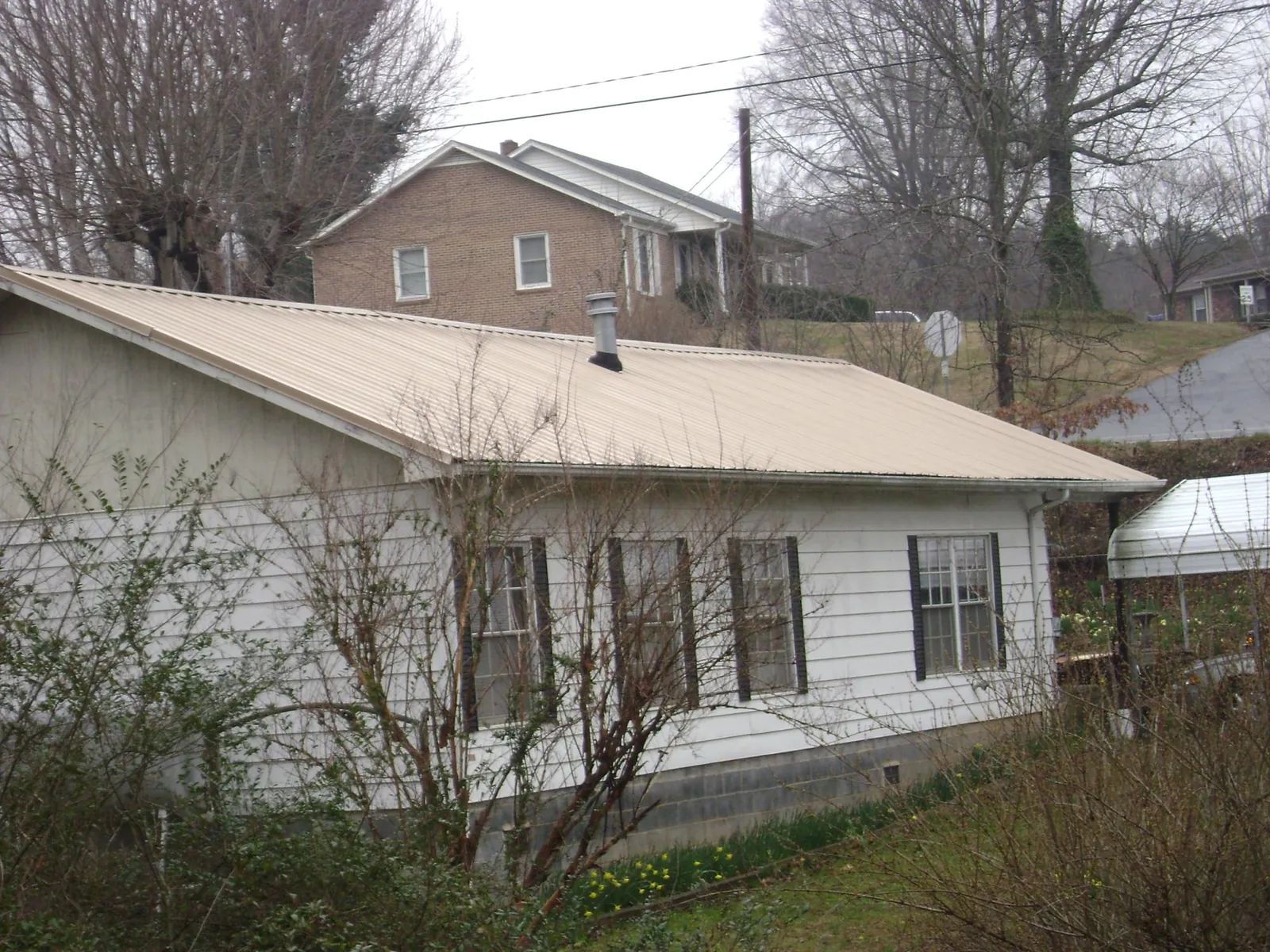 Tan metal roof on a white sided house set into a hillside — Commercial Roofing by Roofing Brothers in De Borgia