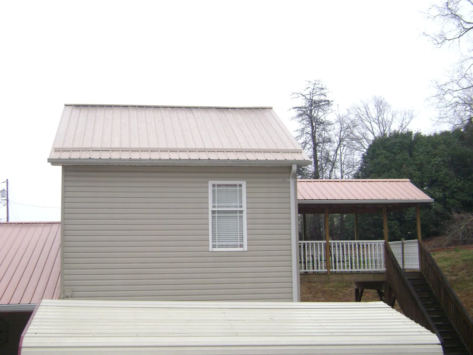 Tan metal roofs on a two story addition and attached porch, from a Roof Replacement job in De Borgia
